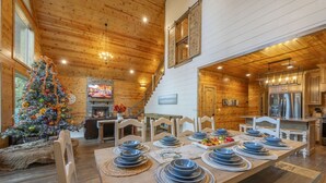 A cozy cabin interior with a dining area set for a meal, a decorated Christmas tree, and a fireplace.