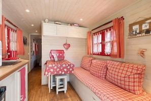 A cozy room with a checkered sofa, a small table with a heart-shaped decoration, and a window with red curtains.