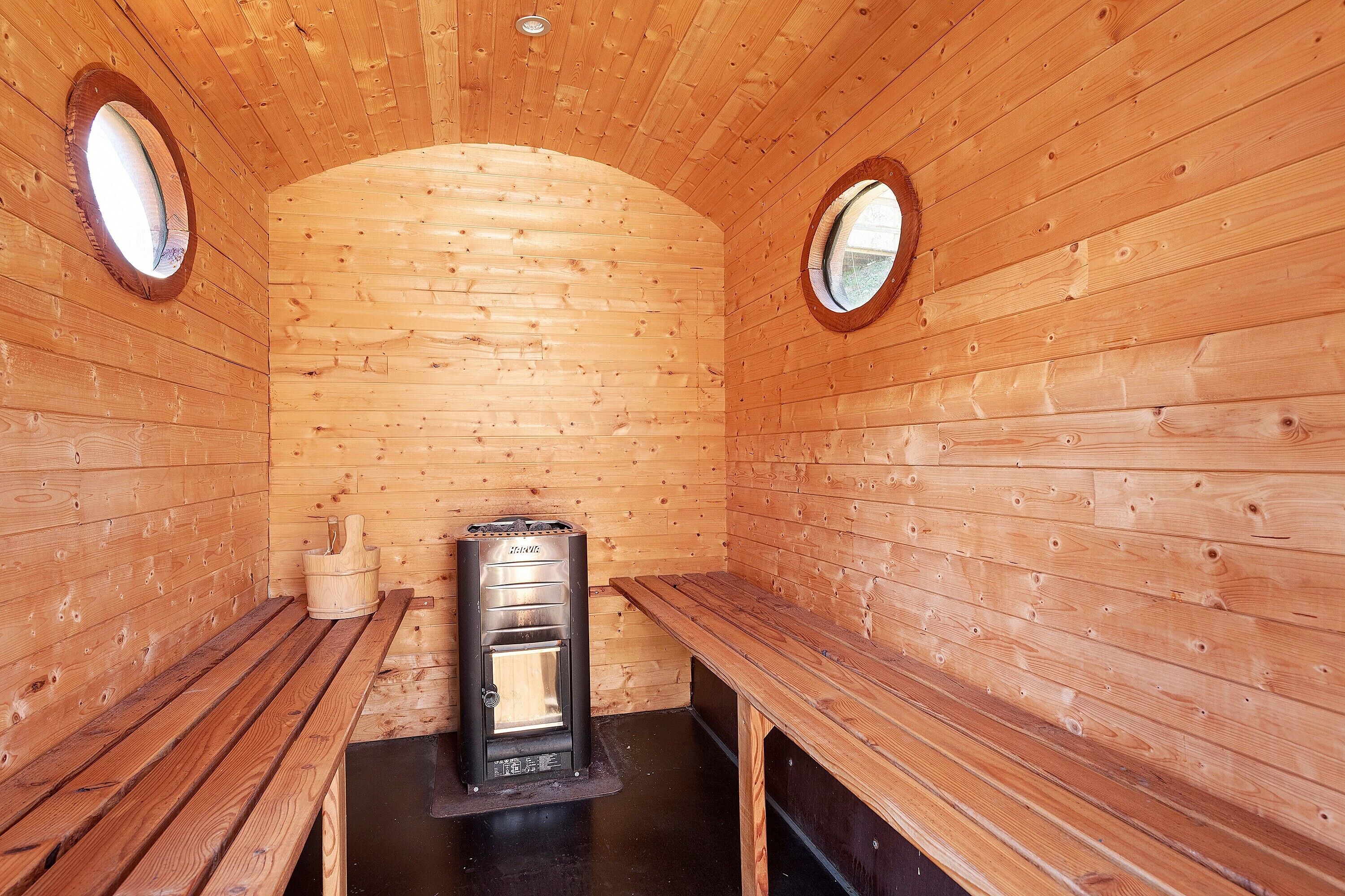 A sauna room with wooden walls, benches, and a sauna unit.