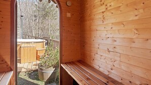 Un sauna en bois, avec un banc, une porte en bois et une vue sur une terrasse en bois et des arbres.