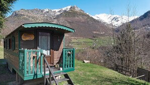 Une cabane en bois avec un toit vert et un escalier en bois menant à l’entrée, le tout se dressant sur fond de montagnes enneigées.