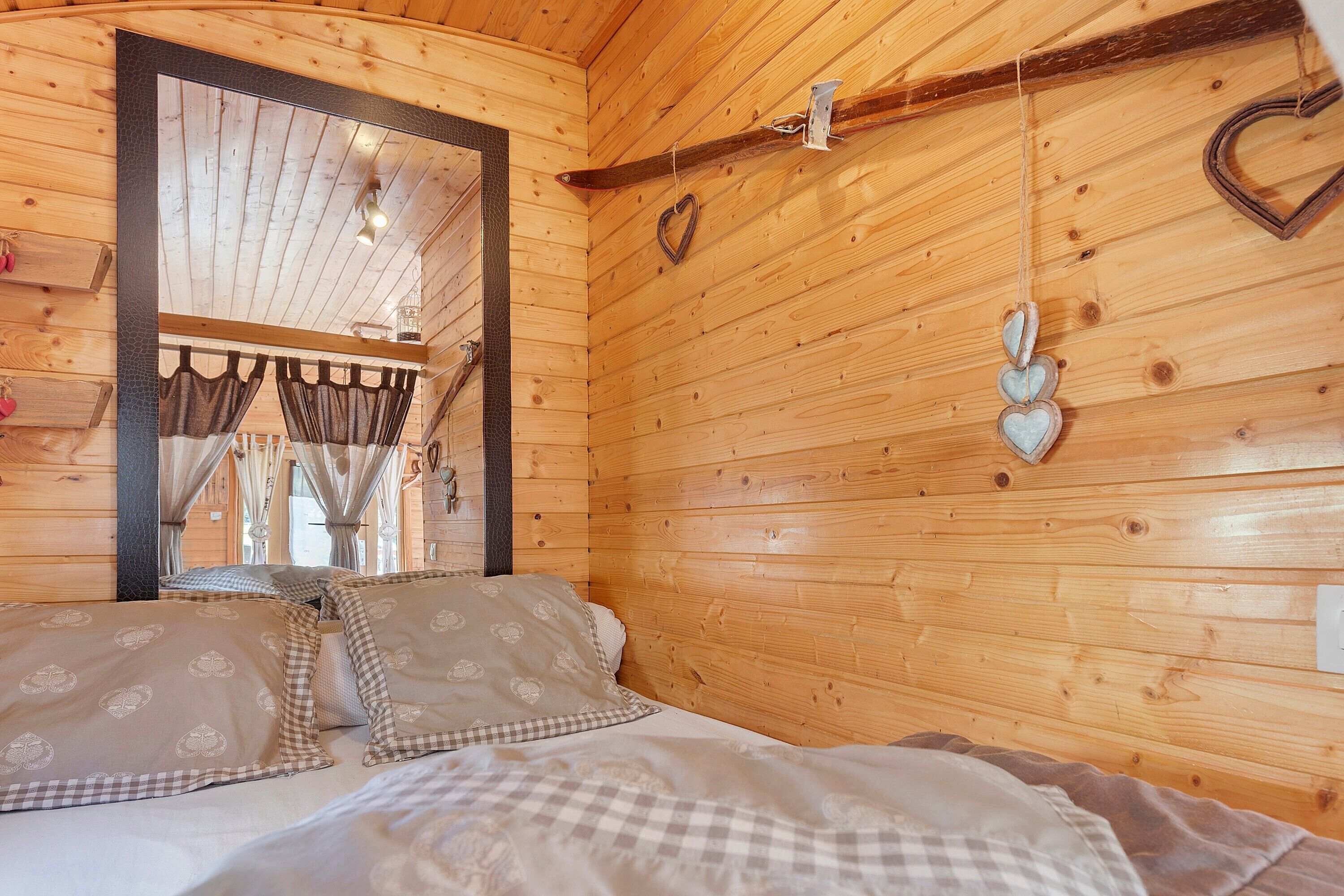 A wooden cabin room with a bed, curtains, and heart-shaped decorations.