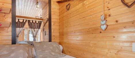 A wooden cabin room with a bed, curtains, and heart-shaped decorations.