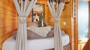 Un dormitorio de cabaña de madera con cama, cortinas y un oso de peluche.