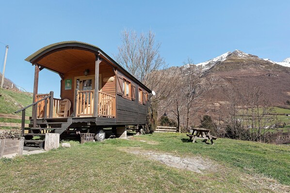 A wooden cabin with a porch, a picnic table, and a mountain backdrop. - Roulotte Edelweiss – Unique Wooden Caravan Stay in Gavarnie (Gavarnie-Gèdre)