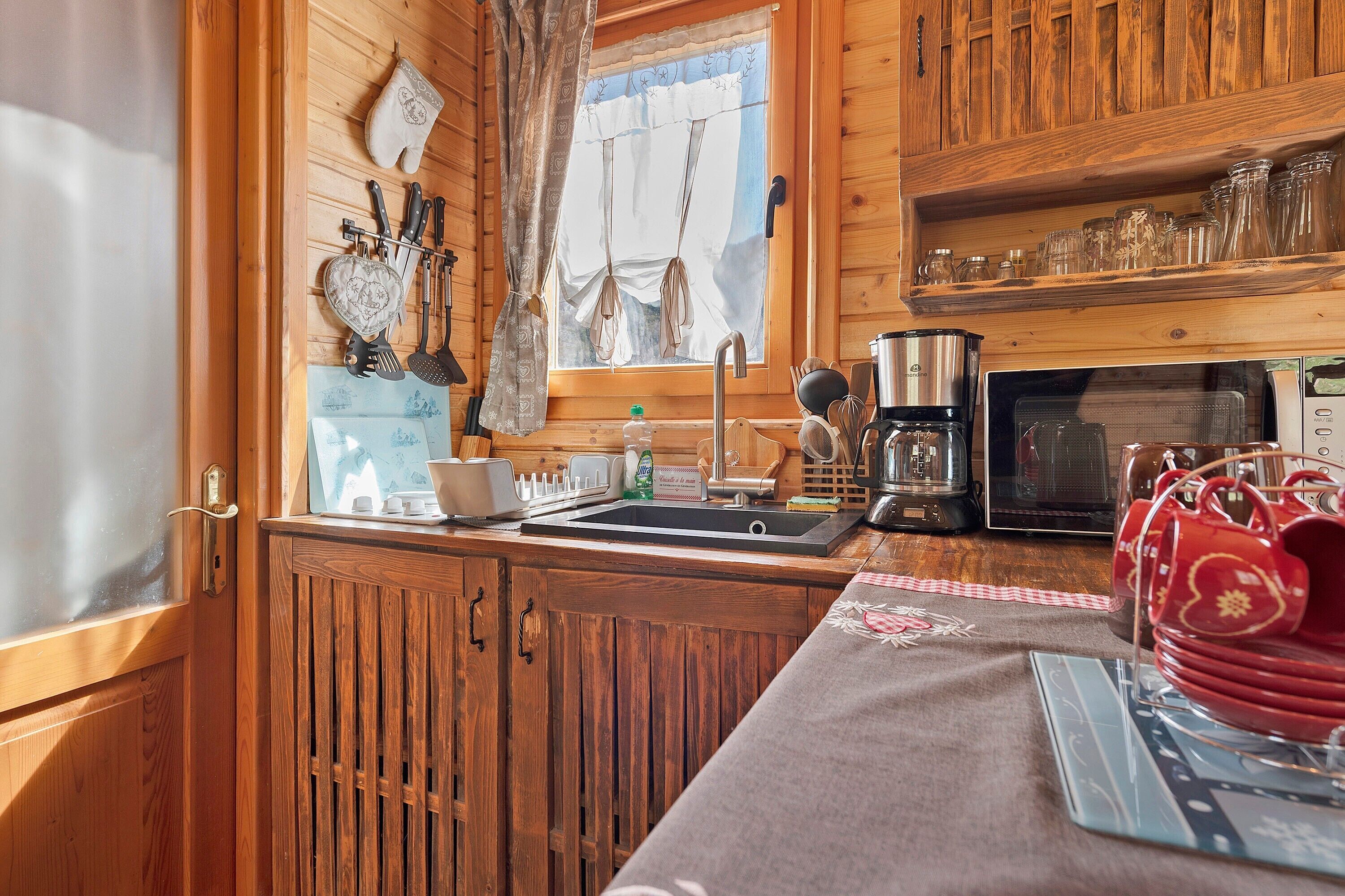 Cocina de cabaña de madera con ventana, armarios de madera, un lavabo, un microondas y diversos utensilios de cocina.
