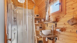 Baño de cabaña de madera con ducha cubierta de vidrio, repisas de madera y un lavamanos blanco.