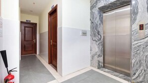 A hallway with a marble wall, an elevator, and a fire extinguisher.