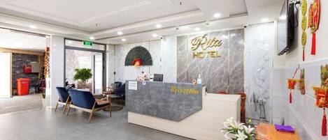 A hotel reception area with a marble reception desk, seating, and a wall-mounted television.
