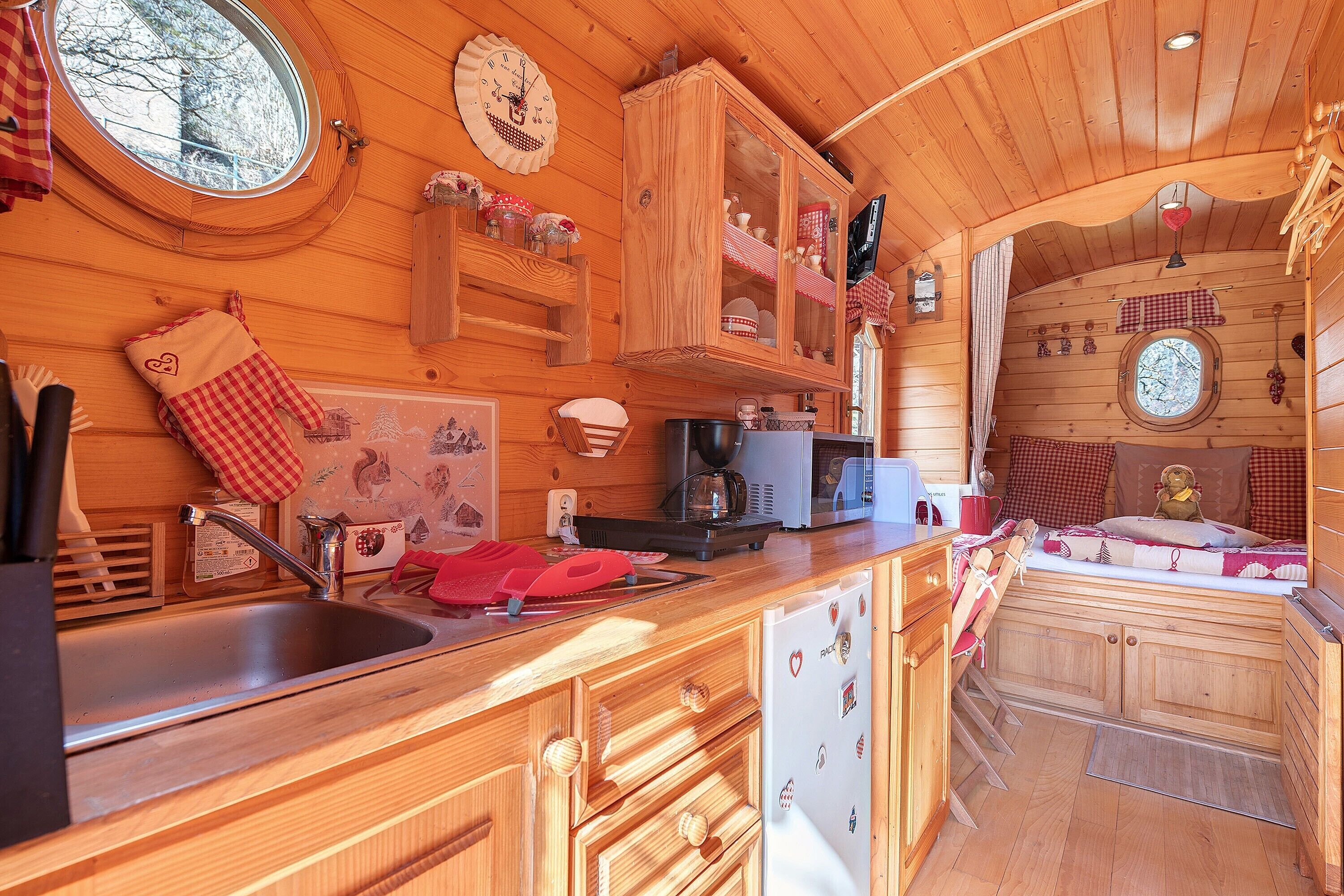 L’intérieur d’une cabane en bois comprend un coin cuisine, des placards en bois, un évier et une fenêtre.