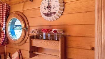 Interior de una cabaña de madera con una ventana redonda, un reloj de pared y una repisa con frascos.