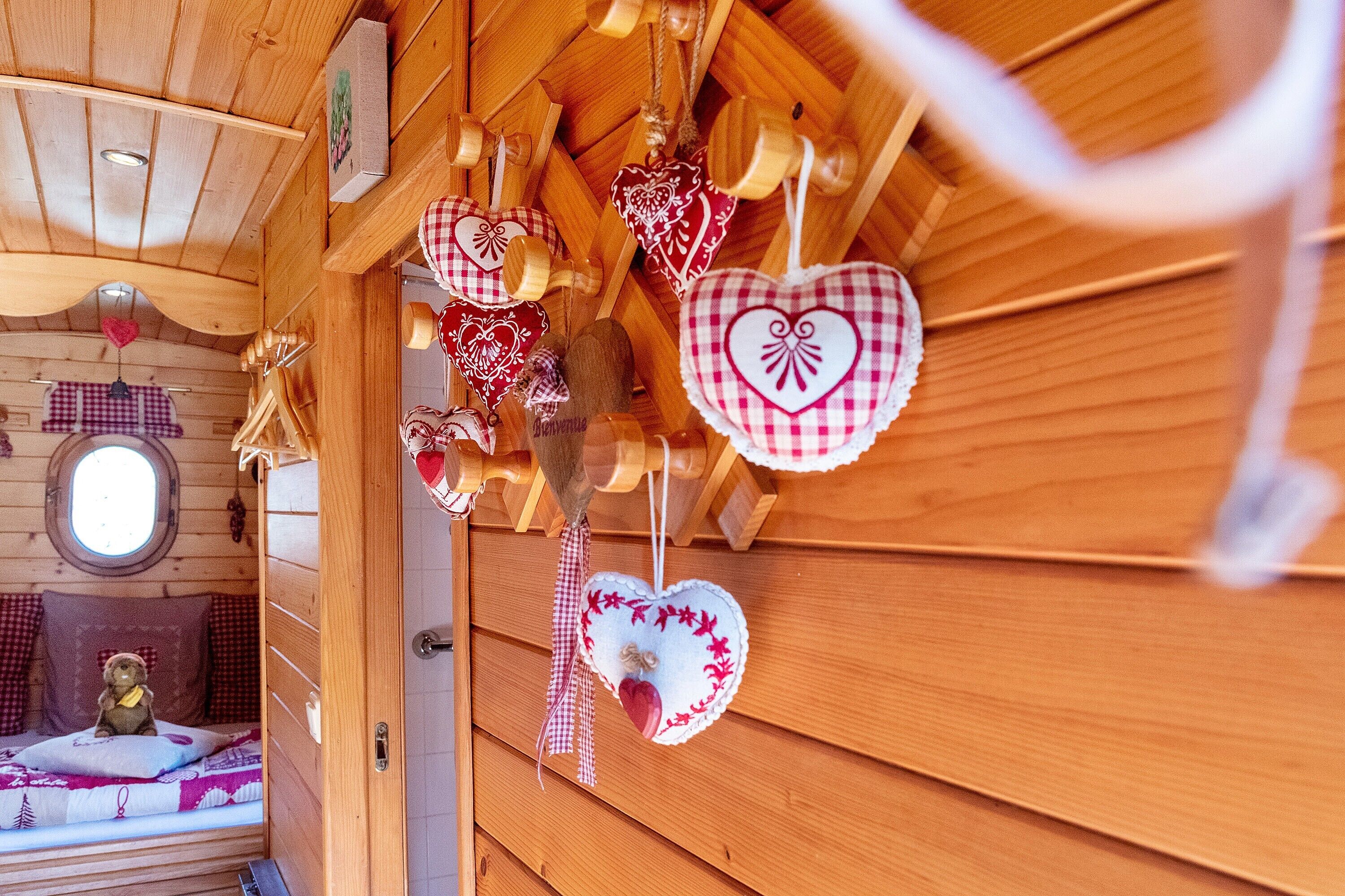 Un interior de madera con adornos con forma de corazón, un osito de peluche en una cama y una ventana.
