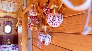 Un interior de madera con adornos con forma de corazón, un osito de peluche en una cama y una ventana.