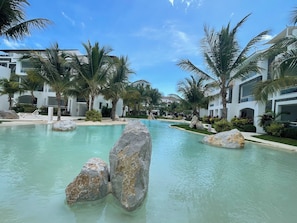 Una piscina di un resort con acqua cristallina, circondata da palme e moderni edifici.