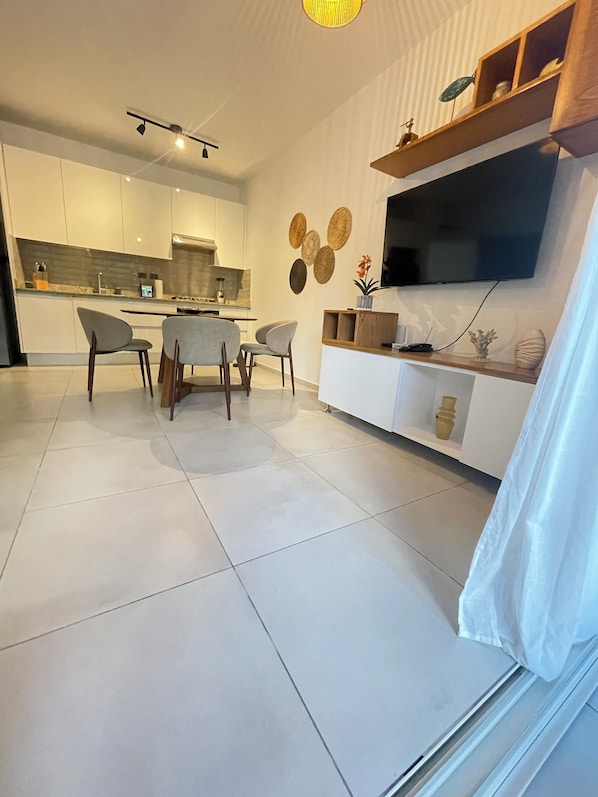 Una cocina moderna con armarios blancos, un comedor con mesa y sillas, y un televisor de pantalla plana montado en la pared.