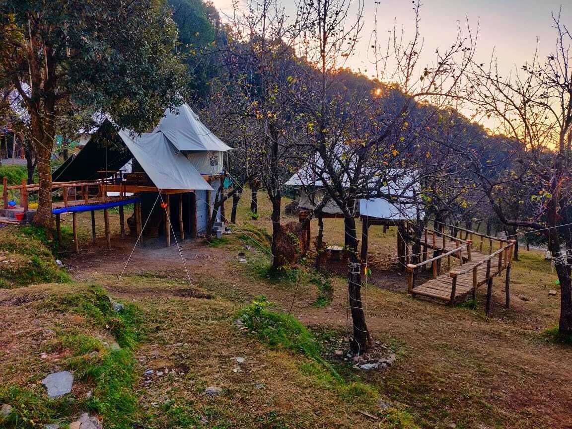Un camping con tiendas de campaña y una estructura de madera, rodeado de árboles y un paisaje montañoso.