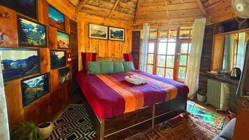 A wooden cabin bedroom with a bed, framed pictures on the walls, and a window with curtains.