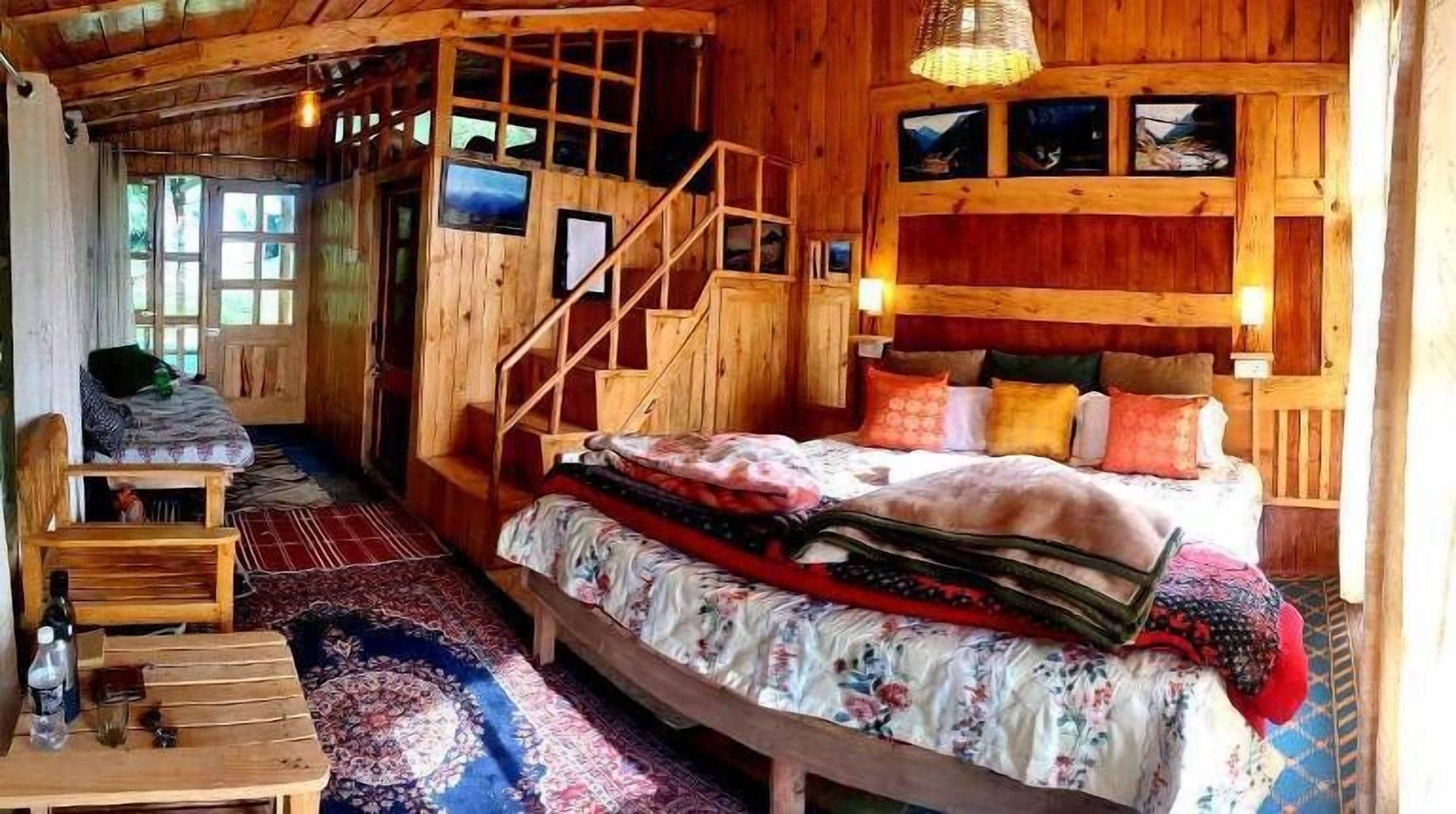 A cozy wooden cabin room with a bed, a chair, a table, and a staircase.