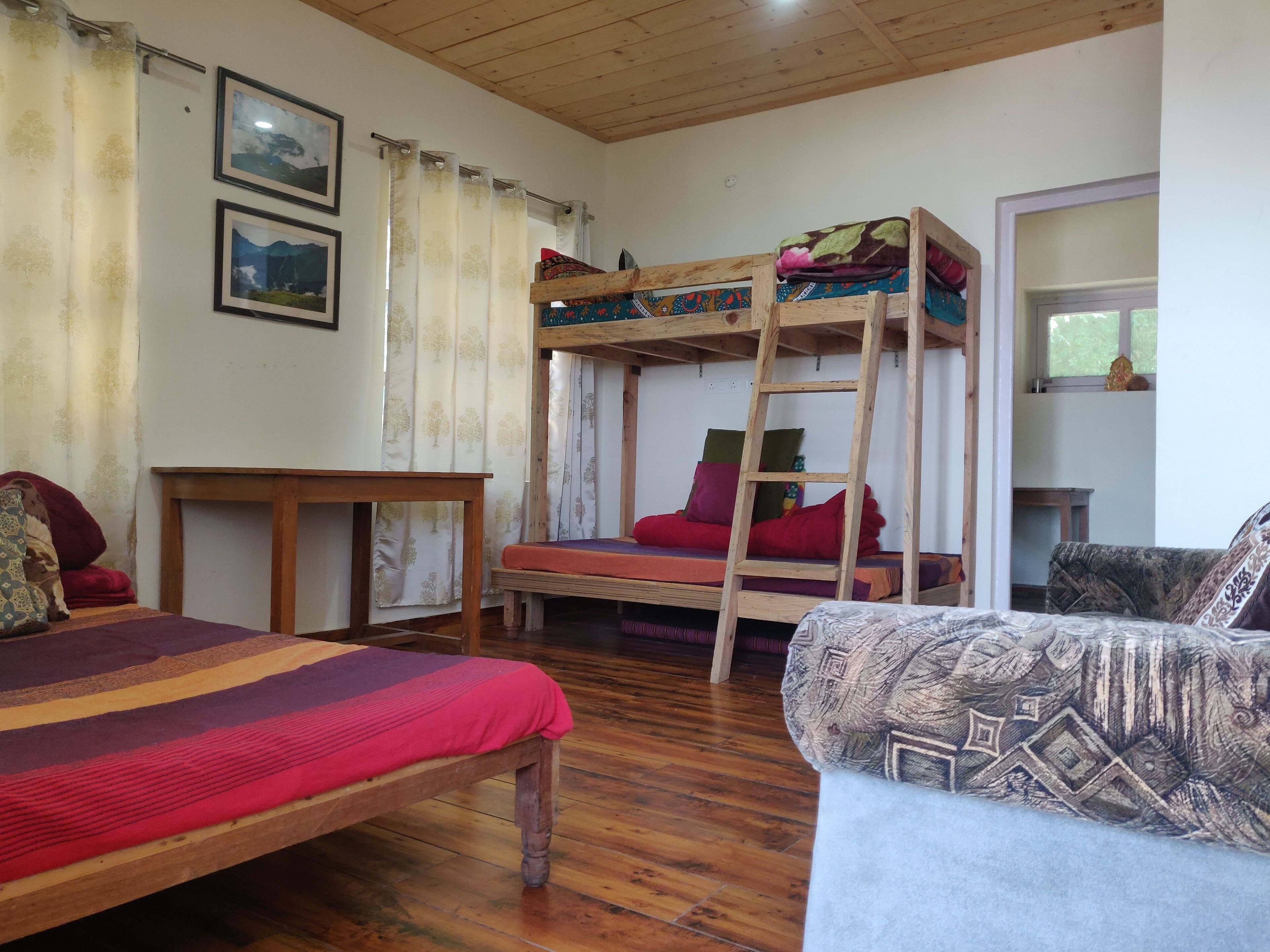 A room with a bunk bed, a sofa, a wooden table, and a bed with a striped blanket.