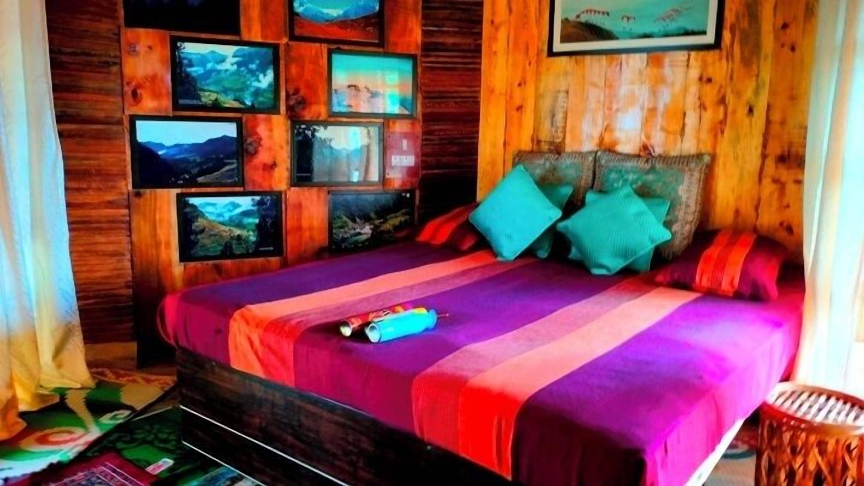 Un dormitorio con pared de madera, una cama con ropa de cama colorida y varias fotografías enmarcadas.