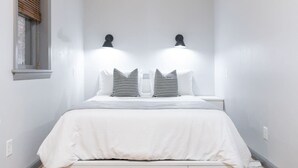 A narrow room with a bed, two wall-mounted lamps, and a window with blinds. - Chic Brownstone in Historic Troy w/Furnished Deck (Troy)