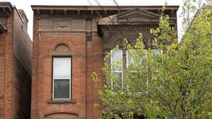 A two-story brick building with a black front door, a small front porch, and a tree in front. - Chic Brownstone in Historic Troy w/Furnished Deck (Troy)