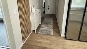 Ein schmaler Flur mit Holzboden, einer weißen Tür am Ende und einem Edelstahlkühlschrank auf der rechten Seite.