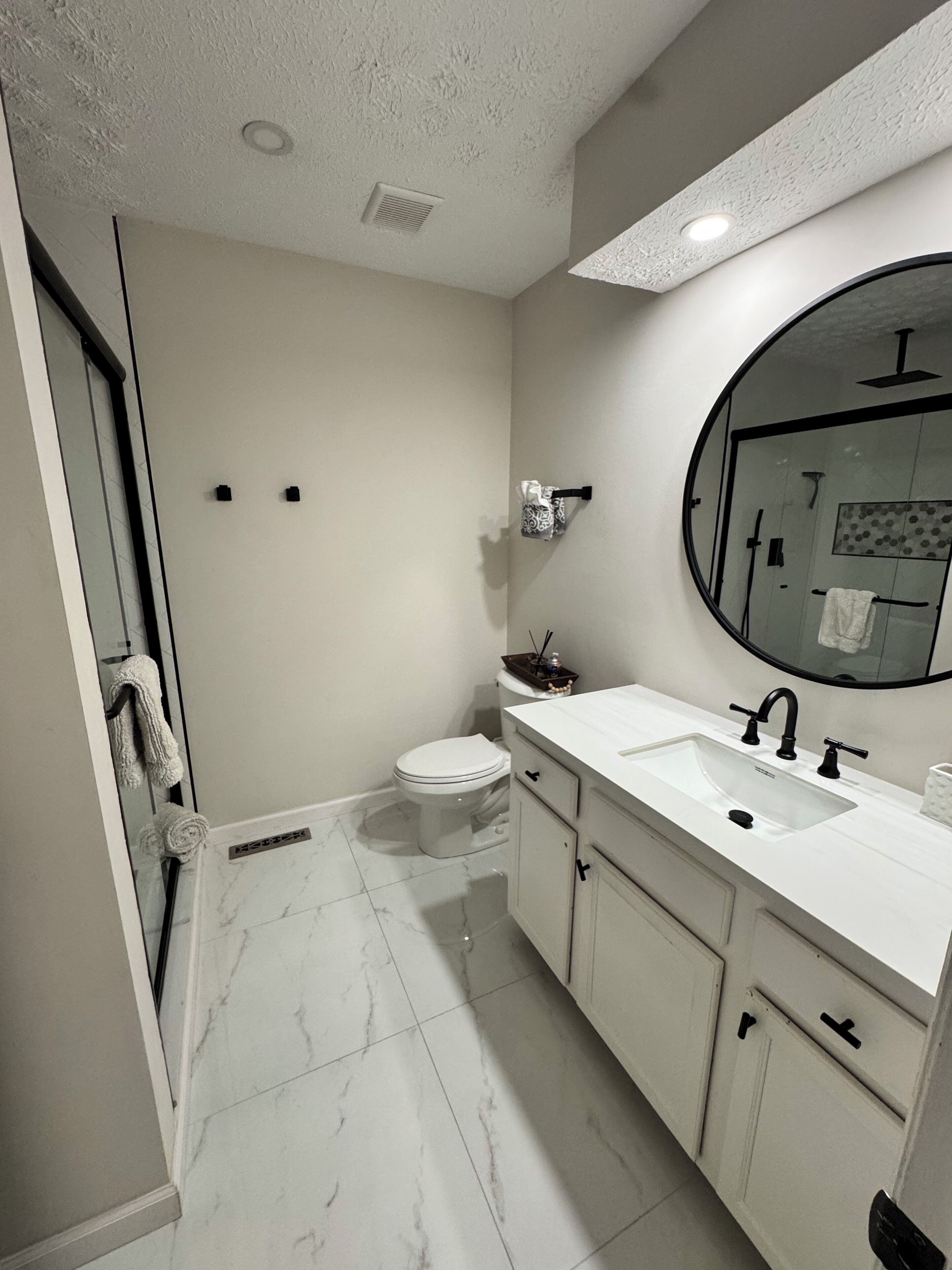 Et moderne badeværelse med et hvidt toilet, en vask med et spejl over, og et bruseområde bag en glassdør.