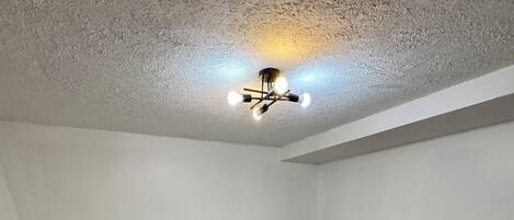 A bedroom with a single bed, a small desk, and a ceiling light fixture.