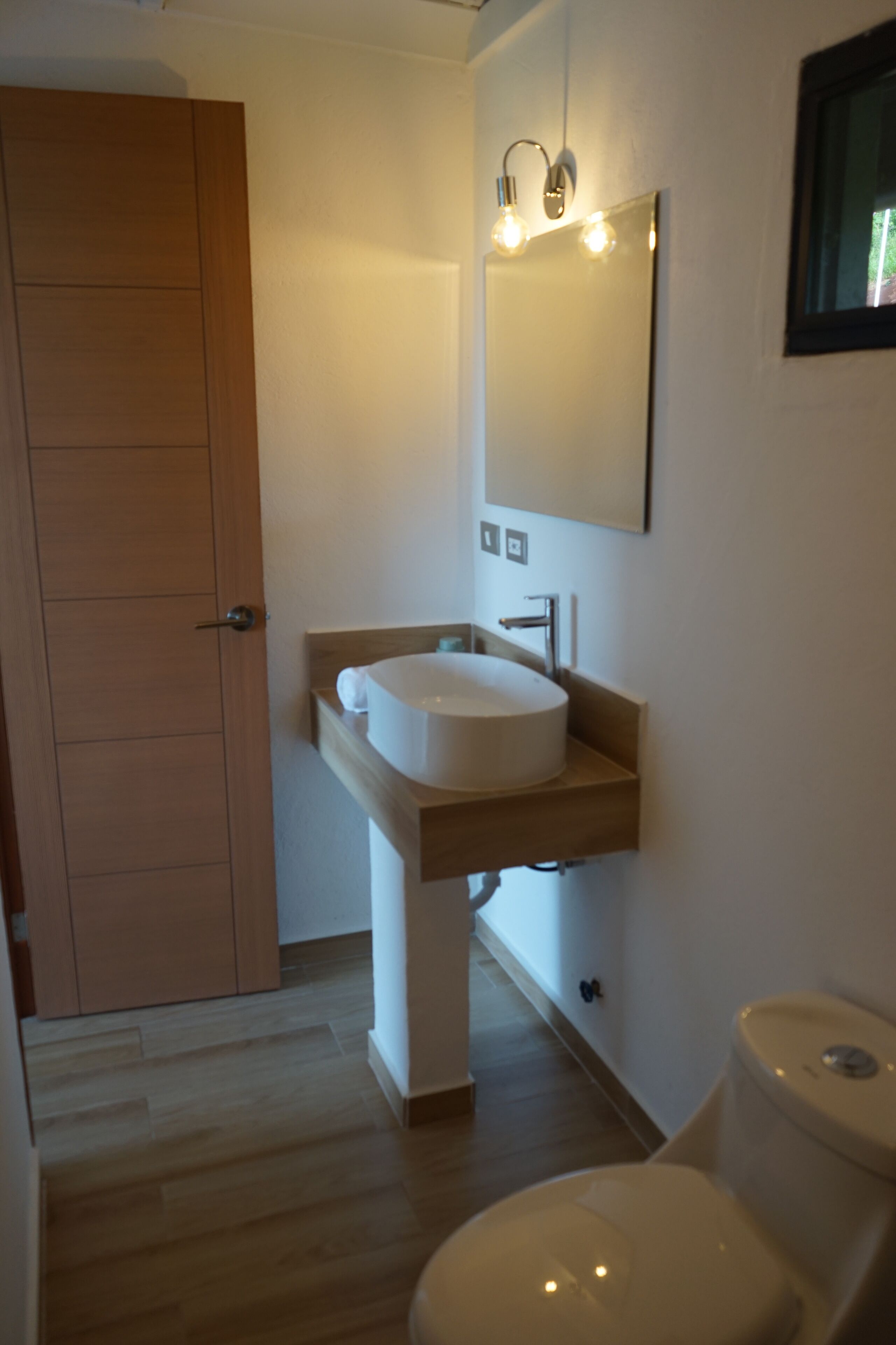 A bathroom with a wooden door, a white sink, a mirror, and a toilet.
