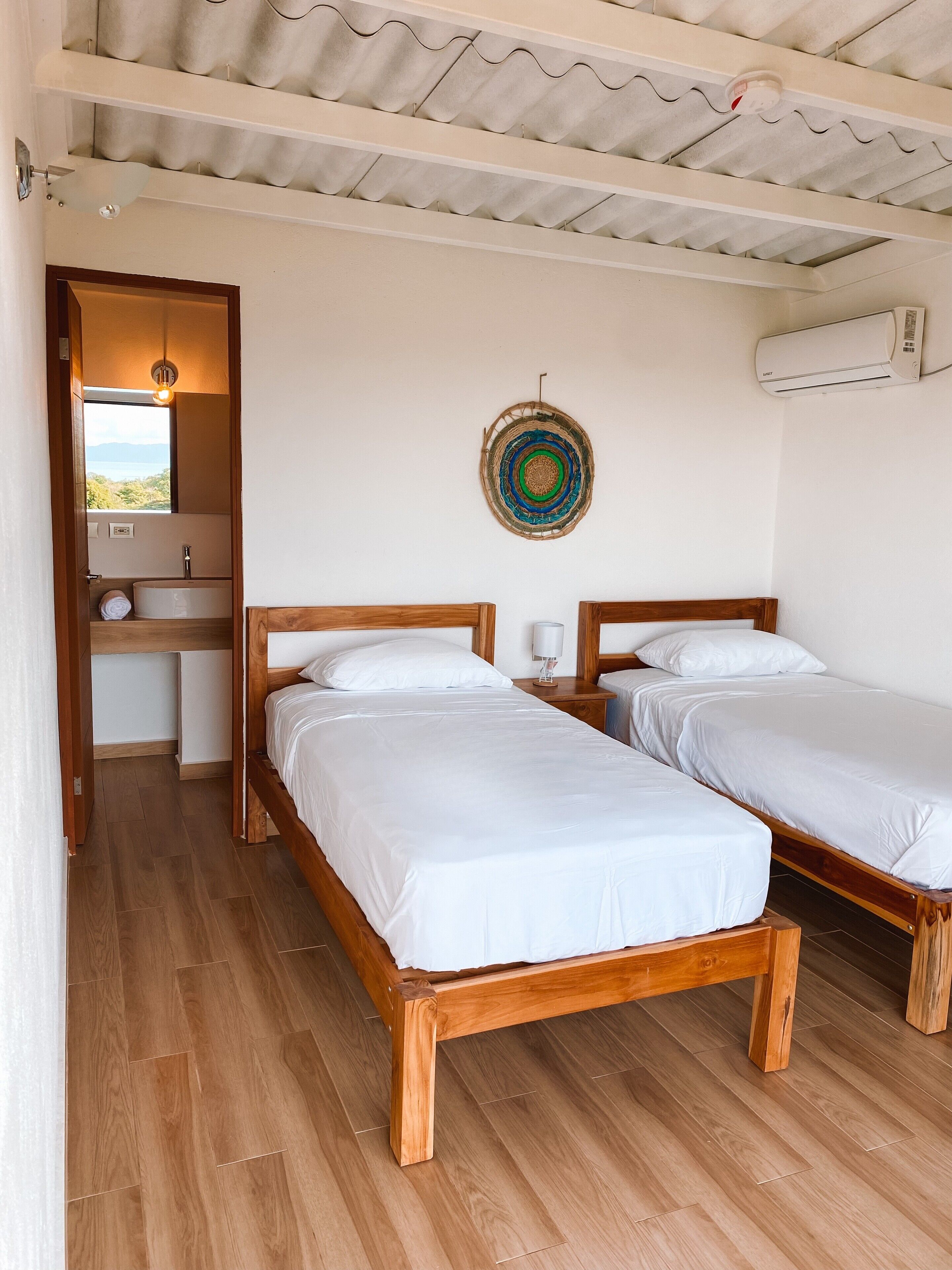 Un dormitorio con dos camas de madera, un baño pequeño y vistas al exterior.