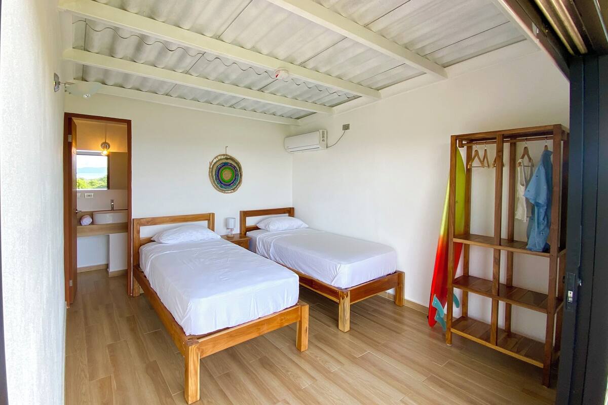 Una stanza con due letti di legno, un armadio in legno e un bagno piccolo con lavandino e specchio.