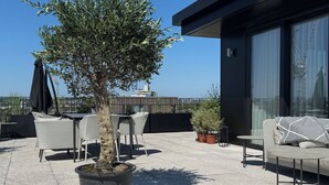 Une terrasse sur le toit, avec des sièges en plein air, un arbre en pot et une vue sur le panorama urbain.