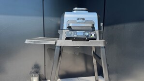 Un barbecue portable, posé sur un support métallique, devant un mur sombre.