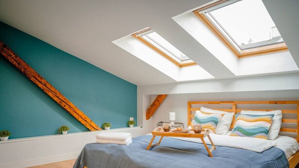 A bedroom with a skylight, a bed with a wooden headboard, and a bedside table with a tray.