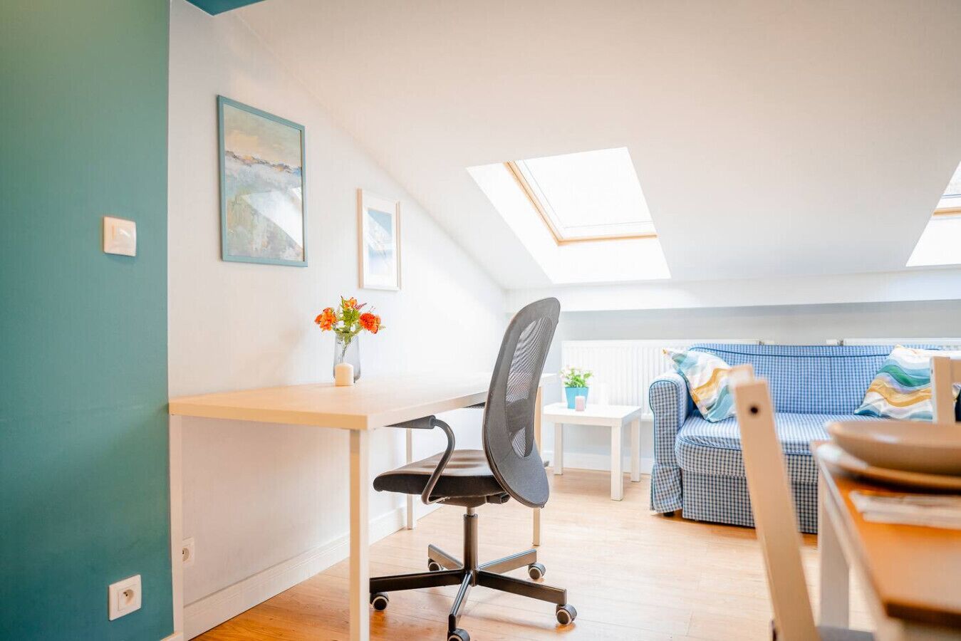 A cozy loft apartment with a desk, chair, and a blue checkered sofa.