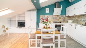 A modern kitchen with white cabinetry, a tiled backsplash, and a dining area with a wooden table and white chairs.