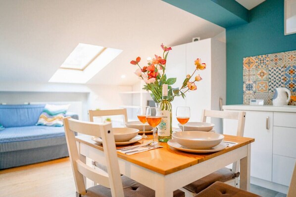 A dining area with a wooden table, chairs, and a vase of flowers. There is a kitchen in the background with a tiled backsplash. - Podgórze Studio - A/C, Workdesk, Castle Nearby (Kraków)