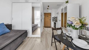 Een moderne, goed verlichte kamer met een grijze bank, een eettafel met stoelen en een keukenruimte zichtbaar door een open deur.