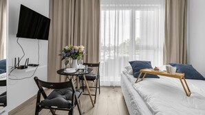 Een moderne hotelkamer met een bed, een eettafel met stoelen, een aan de muur bevestigde televisie en een raam met gordijnen.