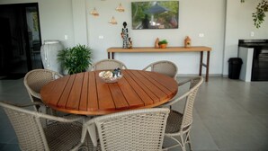 A round wooden dining table with wicker chairs, a vase, and a small decorative item on the table. - Apto c Piscina e 2 su tes a Poucos Passos da Praia (Japaratinga)
