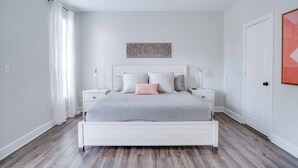 A bedroom with a white bed, two nightstands, a ceiling fan, and a door.