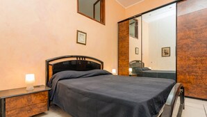 A bedroom with a bed, bedside table, lamp, and a mirror.