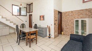 A spacious living area with a dining table, chairs, a sofa, a staircase, and a kitchen area.