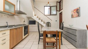 A kitchen with a dining table, chairs, a staircase, and a painting on the wall.