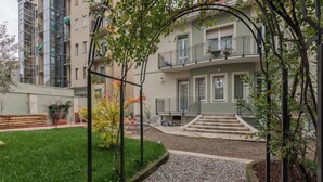 Un edificio residencial con un césped verde, un camino de grava y un balcón con barandilla.