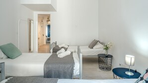 A modern hotel room with a large bed, a smaller bed, a desk, and a chair. There is a window with curtains and a view of the hallway. - Estrela House 3 1 by Homing (Lisbon)