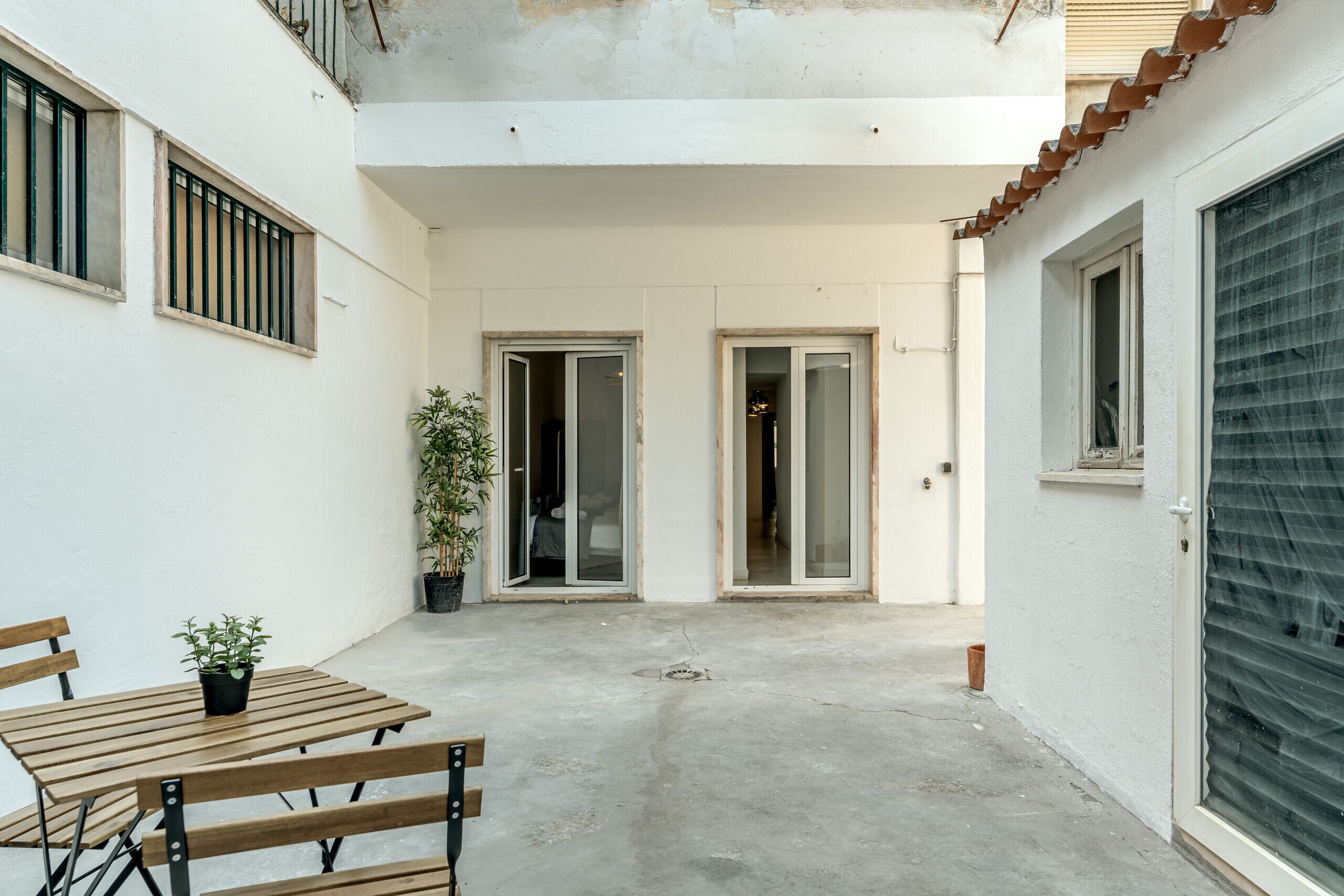 A courtyard with a wooden table and chairs, a potted plant, and a sliding glass door leading to an interior space.