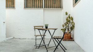A small outdoor patio with a wooden table and two chairs, a potted plant, and barred windows. - Estrela House 3 1 by Homing (Lisbon)