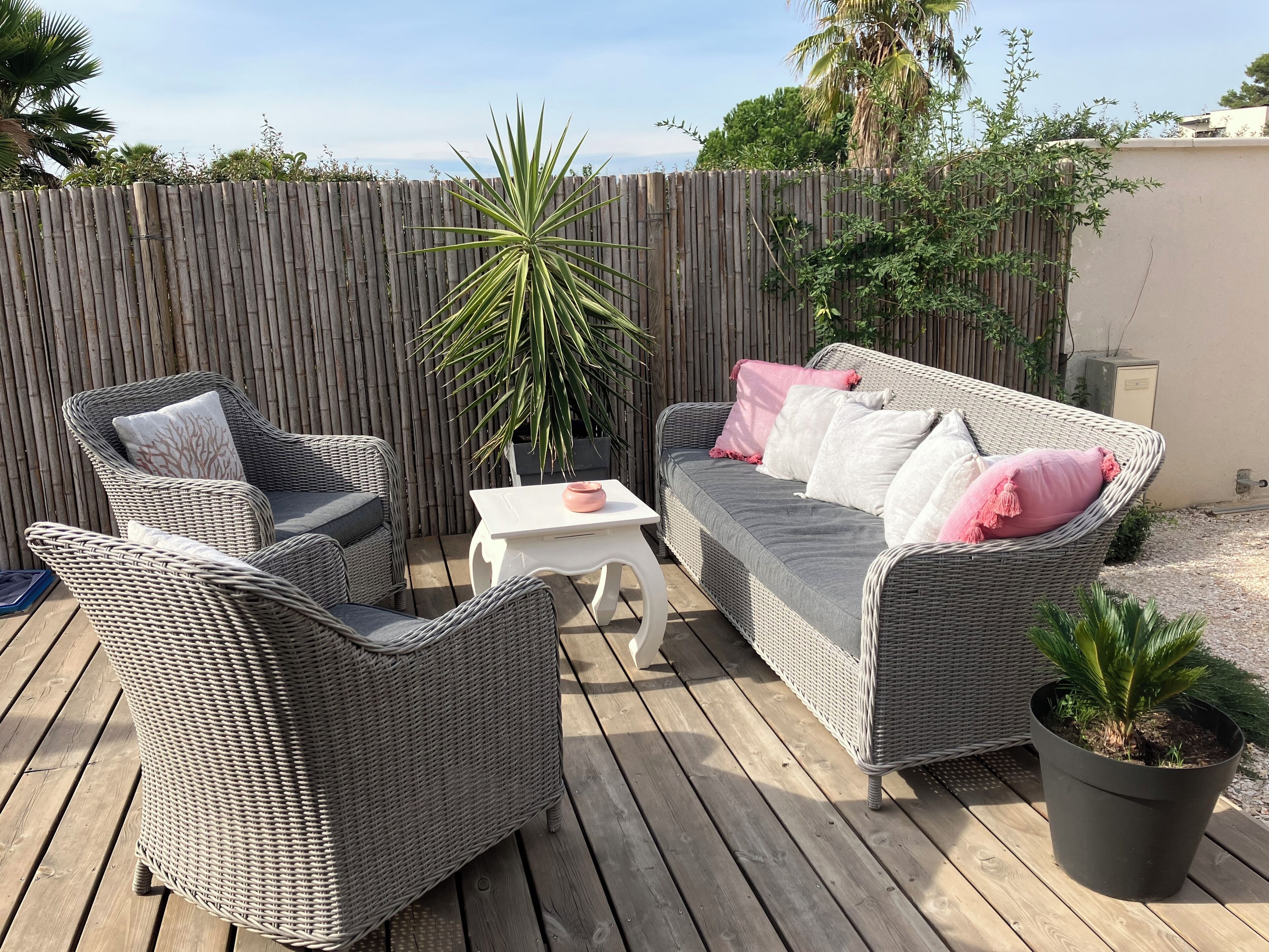 Un patio con mobiliario de mimbre, una mesa blanca y una planta en maceta.